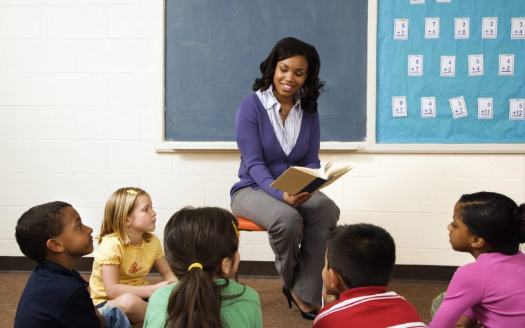 Teacher reading book to young students in classroom. Horizontally framed shot.