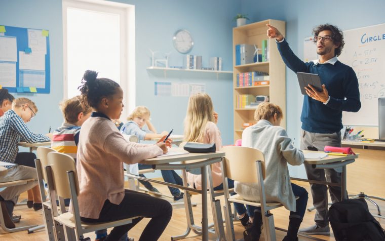 Enthusiastic Teacher Giving a Lesson in Elementary School to Class Full of of Diverse Children. Group of Smart Multiethnic Kids Learning New Stuff. Side View Shot